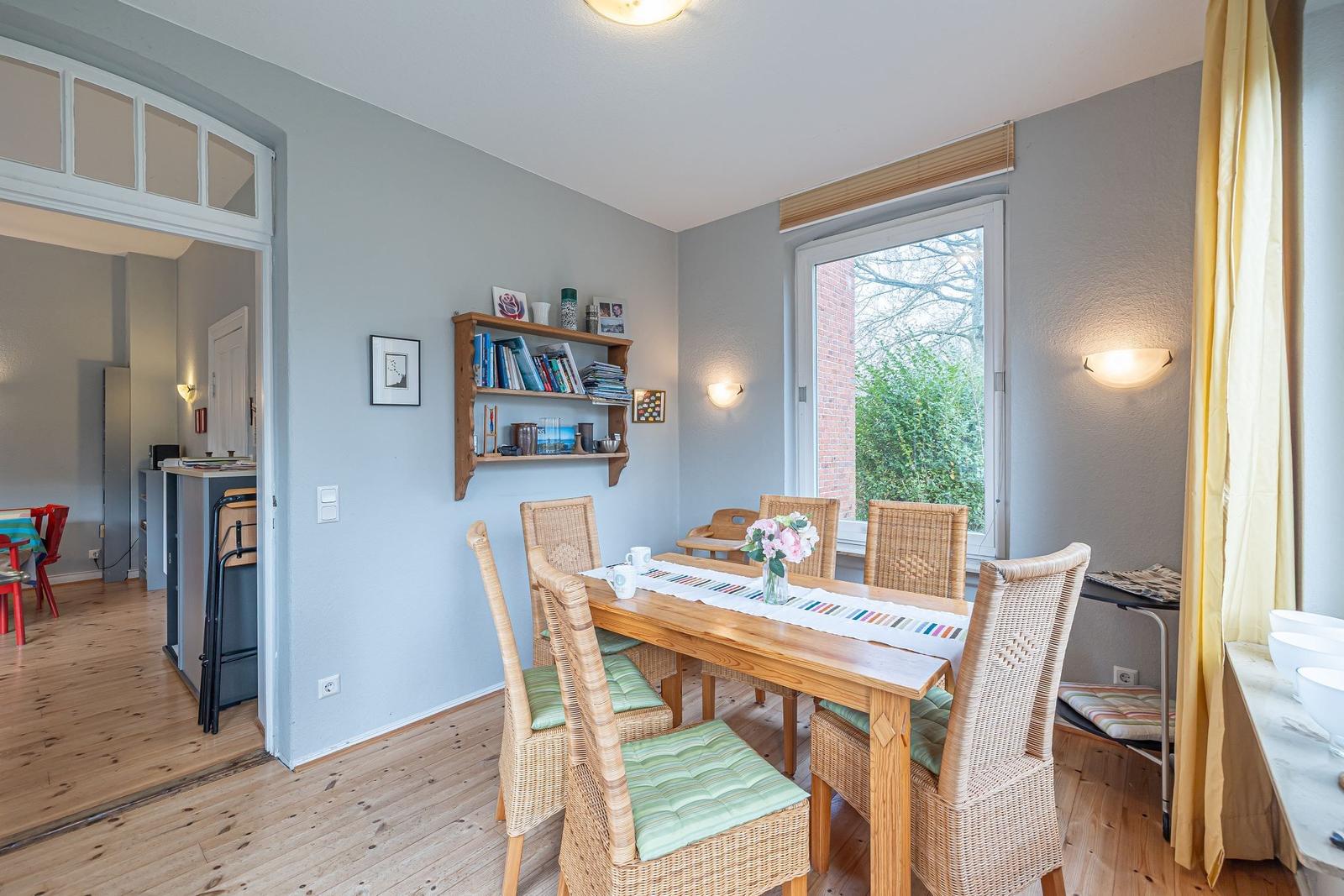 Esszimmer mit Holztisch, Rattanchairs und Fensterblick auf Garten.