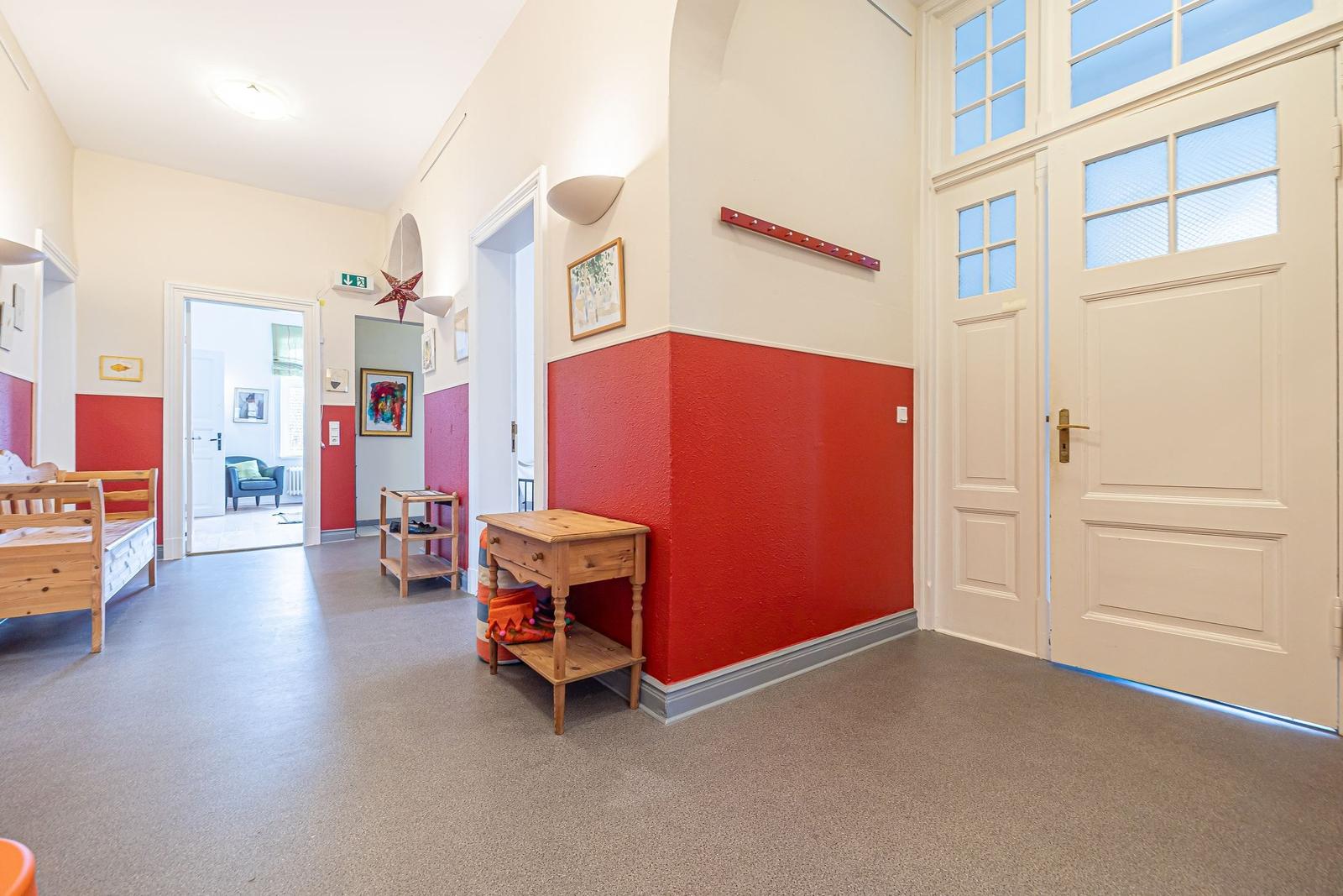 Flur mit rotem Wandabschnitt, Holzmöbel und Türen mit Glasfenstern.