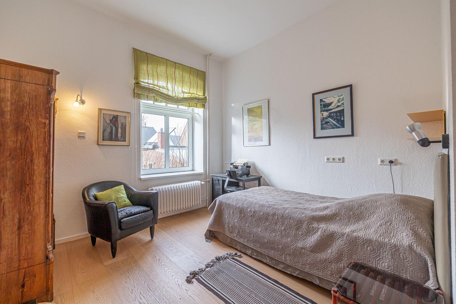 Schlafzimmer mit Bett, Schreibtisch, Stuhl und Holzschrank. Fenster mit grünem Rollladen.