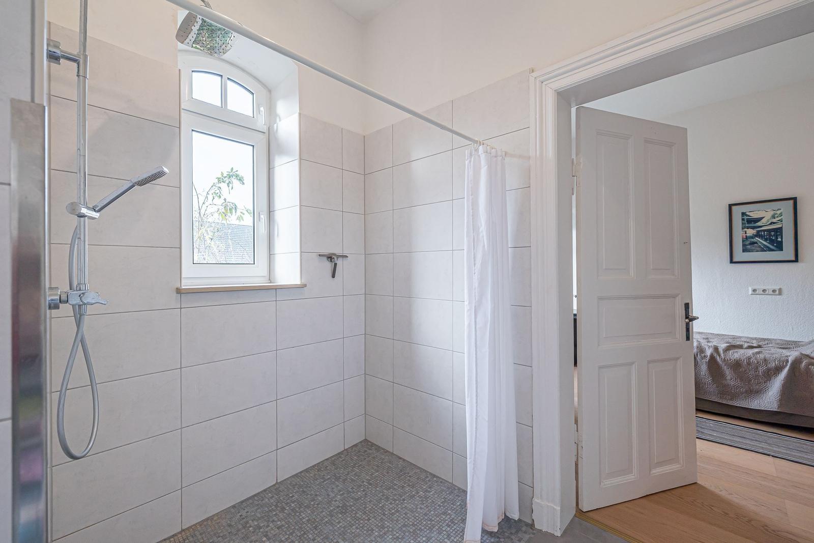 Badezimmer mit Dusche, Fenster und Blick in Schlafzimmer.