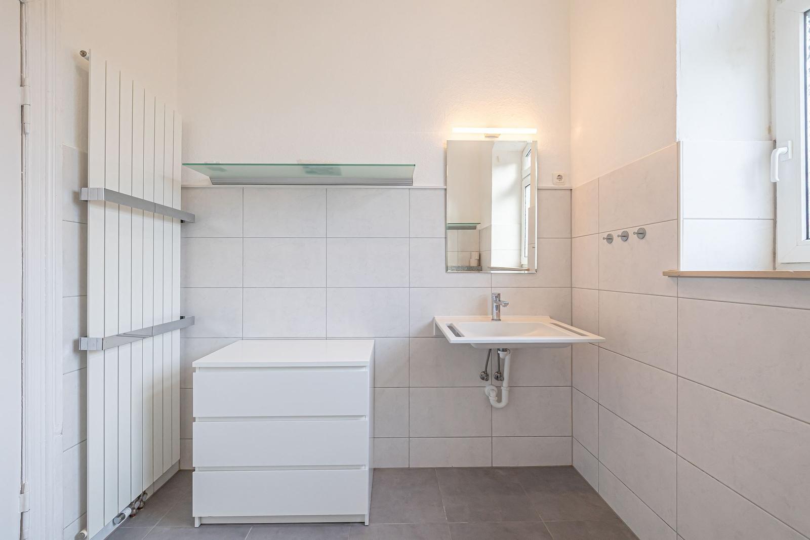 Badezimmer mit Waschbecken, Spiegel und Heizkörper an der Wand.
