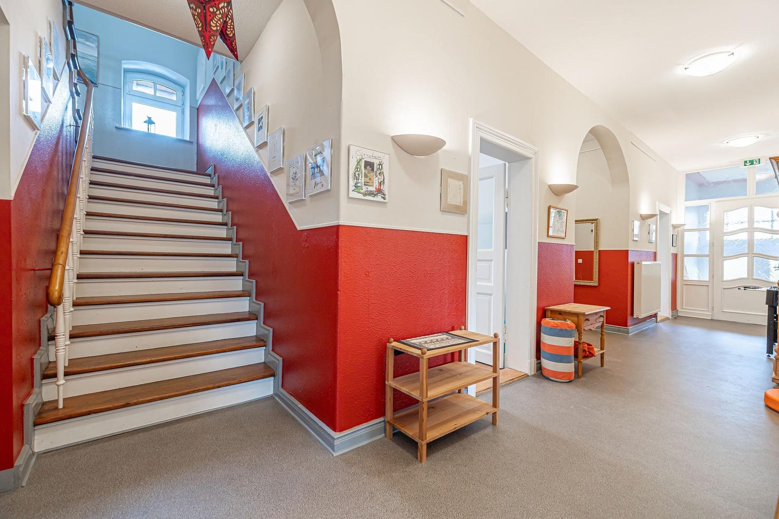 Hausflur mit Treppe, roten Wänden und Holzmöbeln.