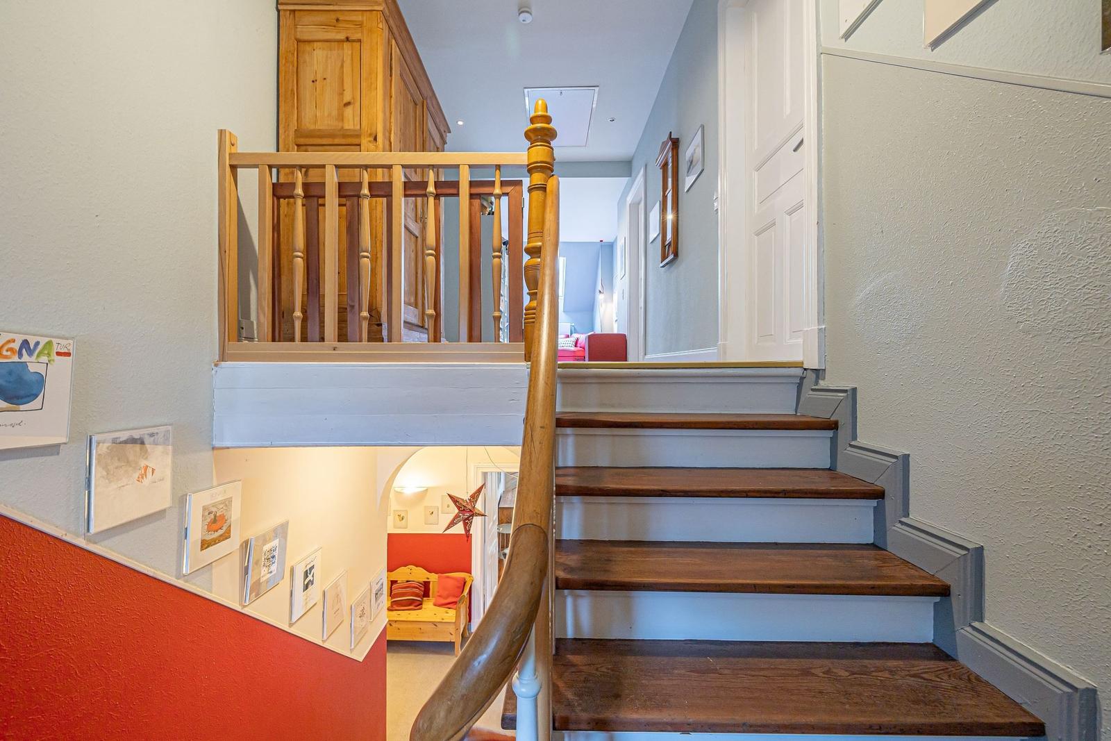 Holzgetreppe mit Geländer führt zur oberen Etage. Unterhalb befindet sich ein Raum mit roter Wand.