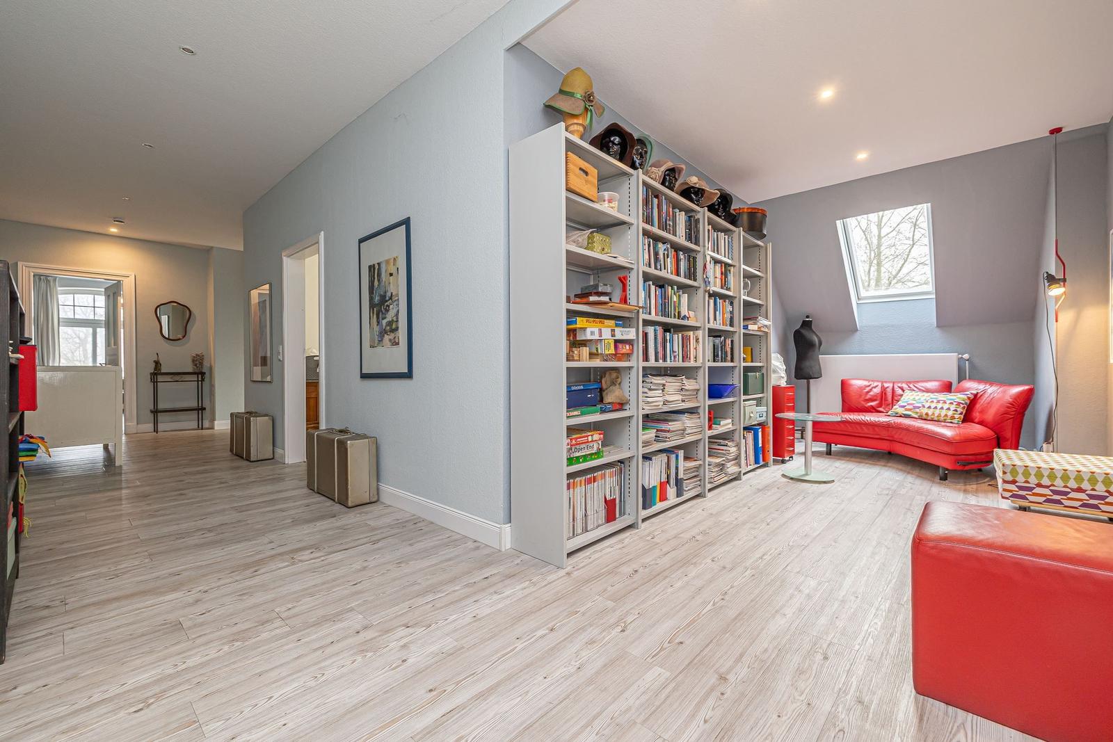 Großes Wohnzimmer mit Bücherregalen, rotem Sofa und Holzboden.