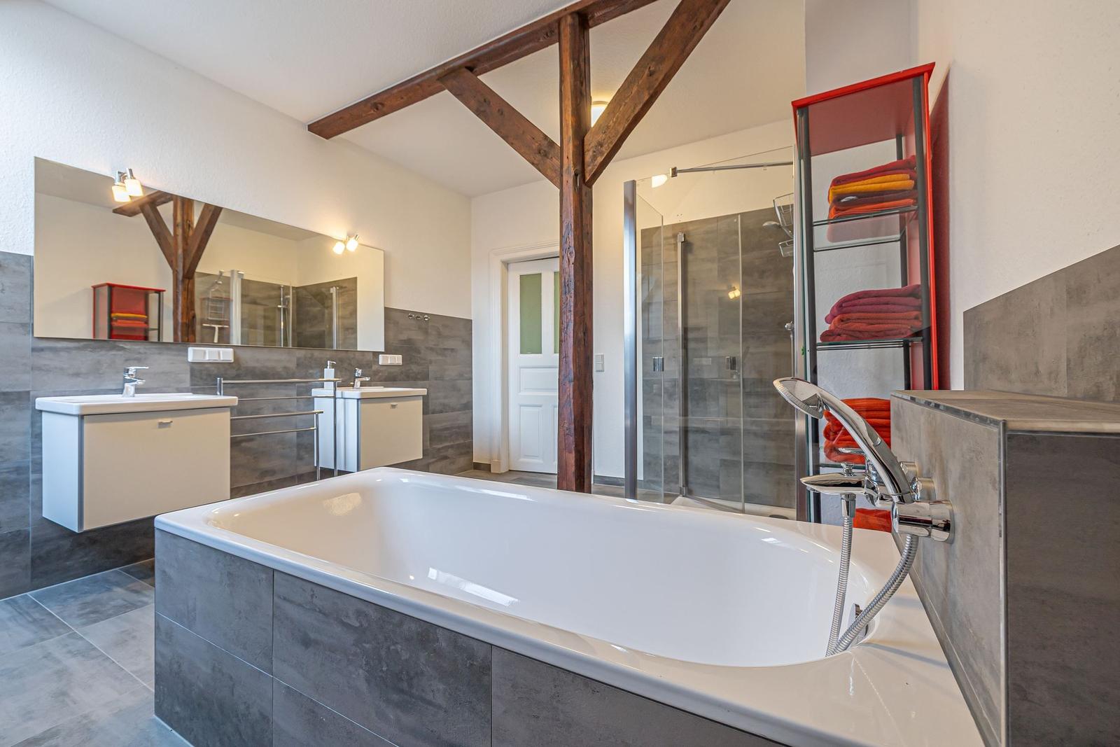 Badezimmer mit Badewanne, Dusche und Waschbecken. Holzbalken und roter Handtuchhalter.