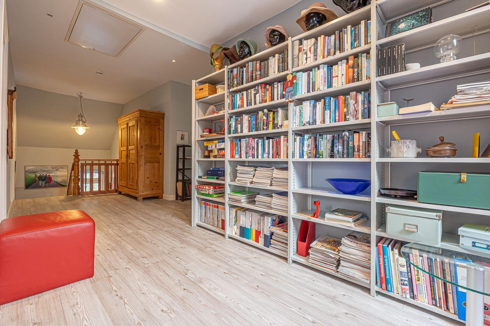 Große Bibliothek mit Bücherregalen, rotem Sitzkissen und Holzfußboden.