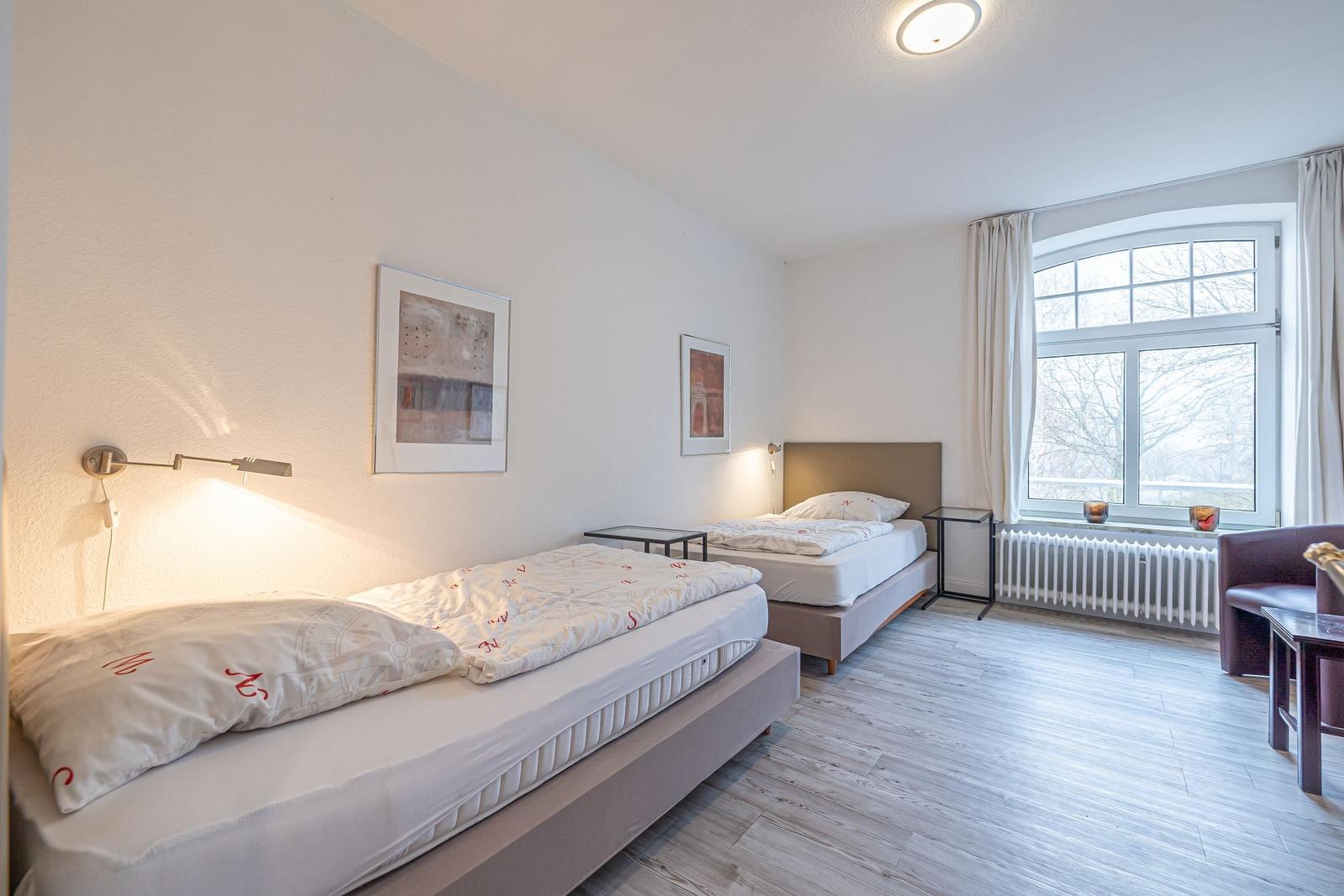 Zwei Betten, Fenster mit Blick, Wandbilder, Beleuchtung und Holzboden.