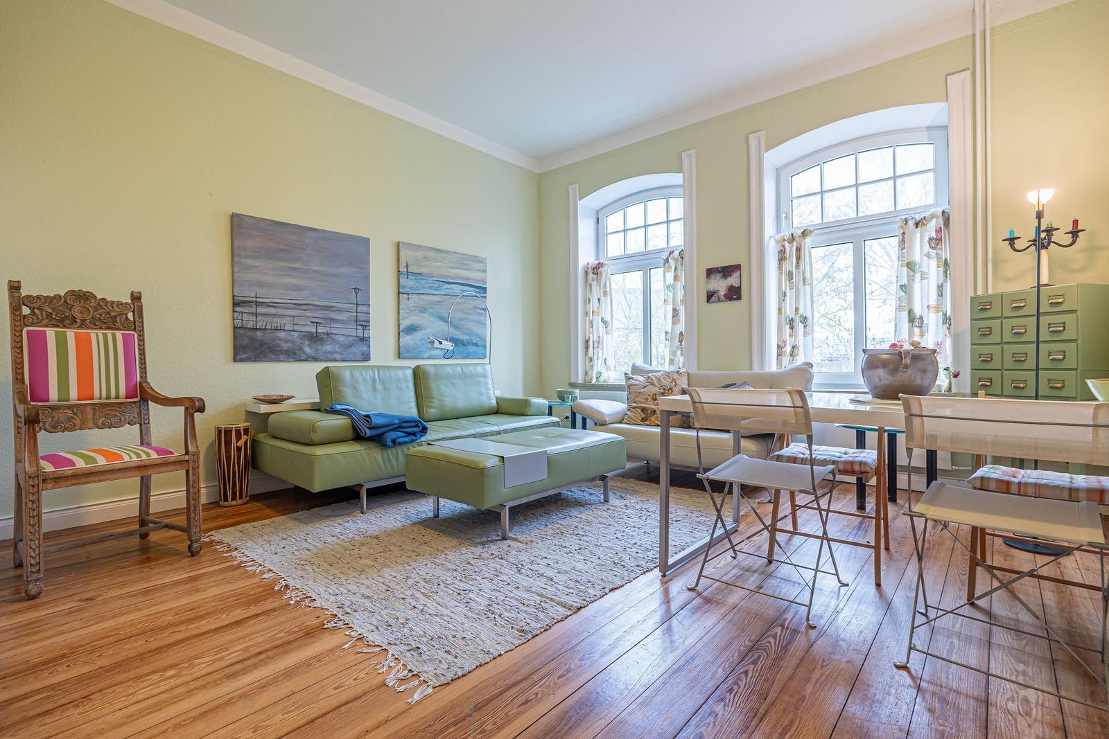 Wohn- und Essbereich mit grünem Sofa, Holzboden und großen Fenstern.