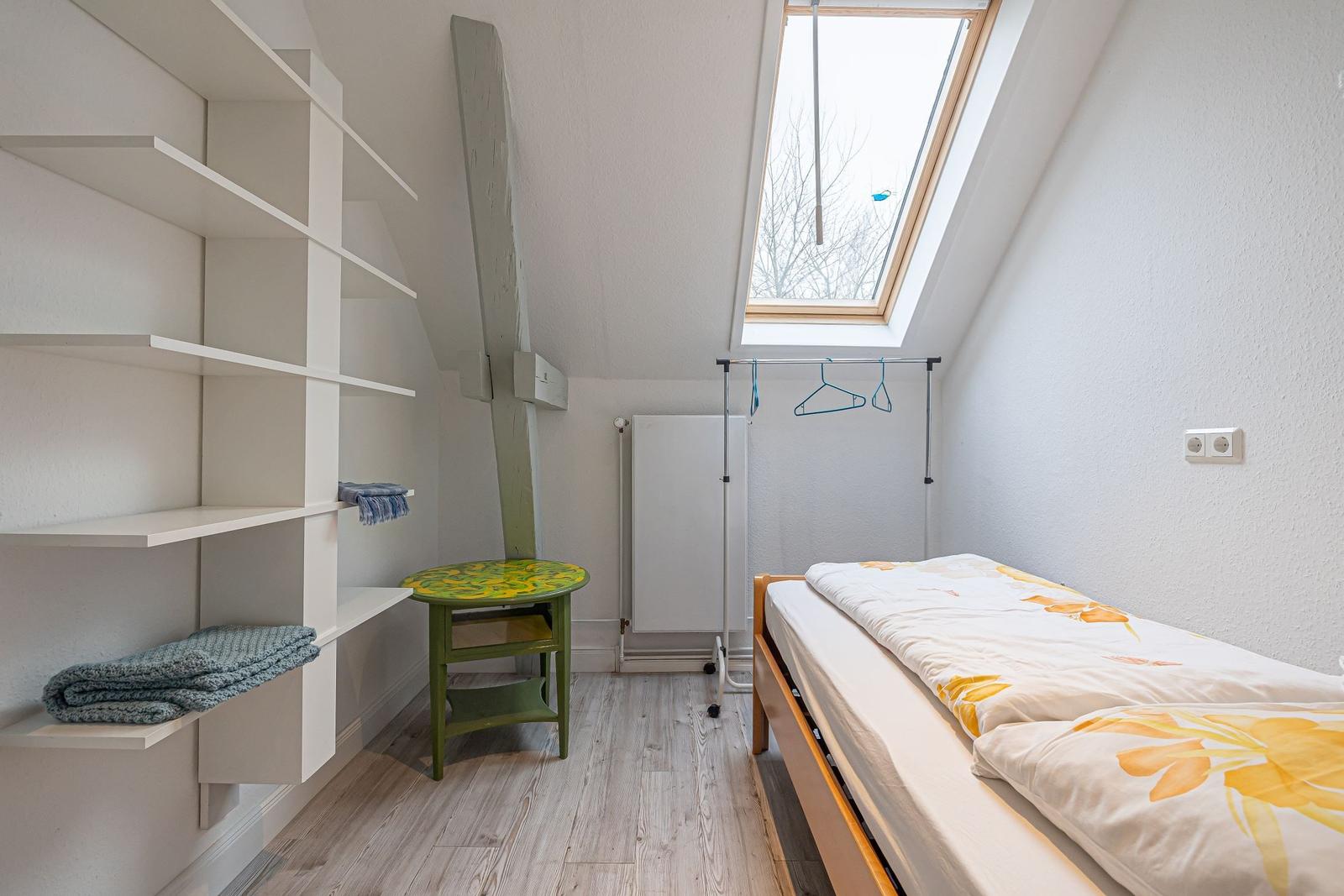 Schlafzimmer mit Dachfenster, Bett, Kleiderständer und Regalwand.