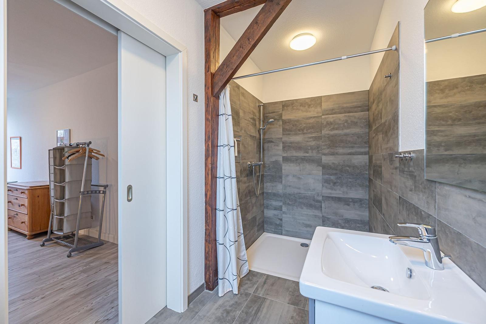 Badezimmer mit Dusche, Waschbecken und Blick in Schlafzimmer.