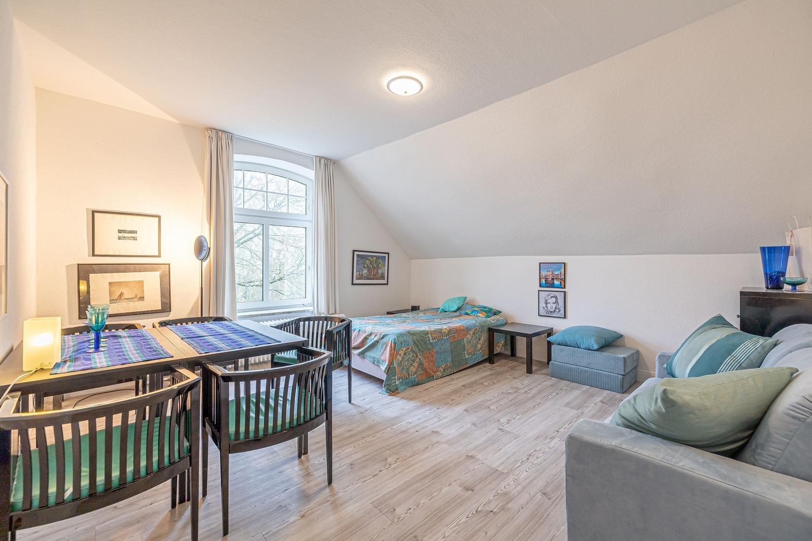 Zimmer mit Schlafplatz, Sitzgelegenheit und Esstisch unter Dachschrägen.