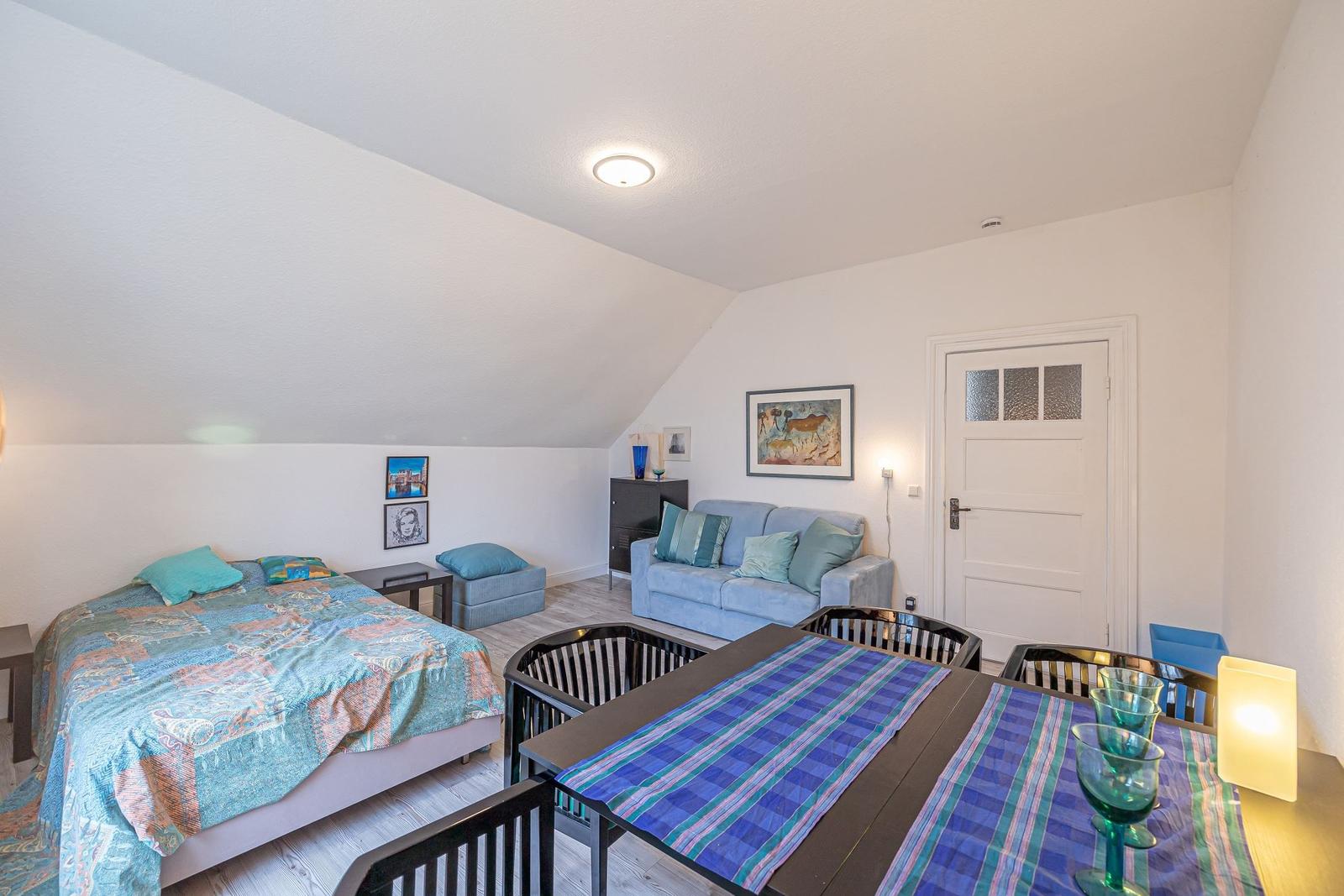 Schlafzimmer mit Sofa, Tisch und Bett unter Dachschrägen.