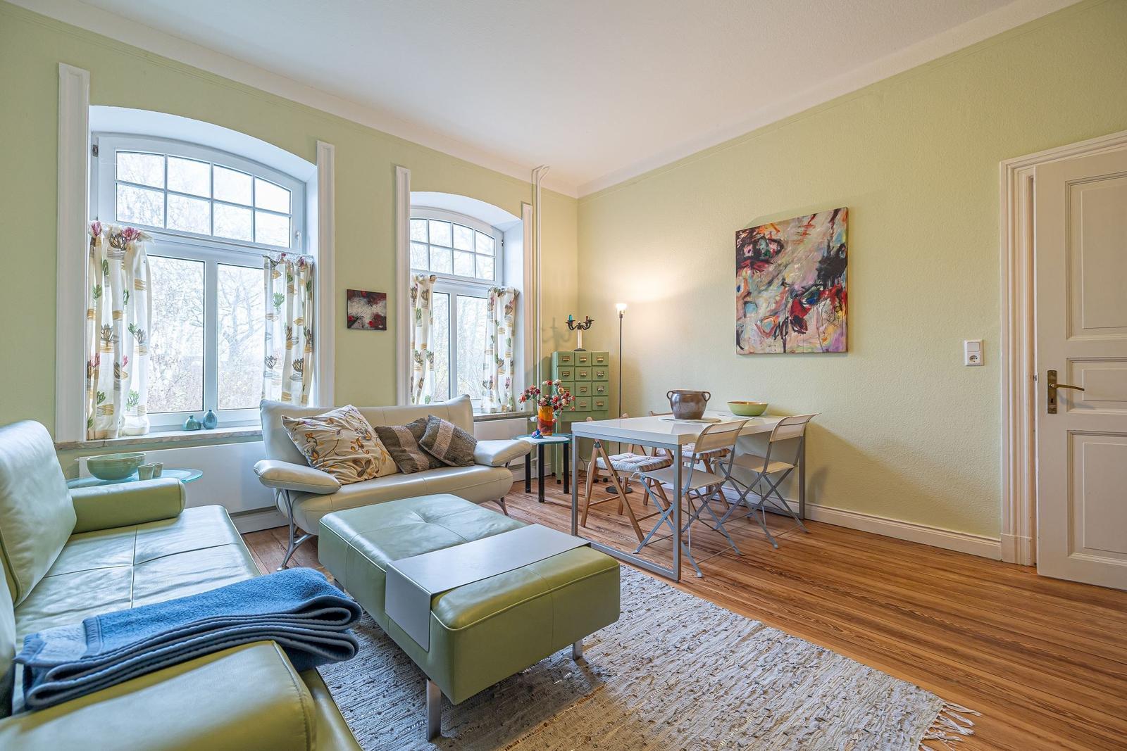 Wohn- und Essbereich mit grünem Sofa, Holzboden und zwei Bogenfenstern.