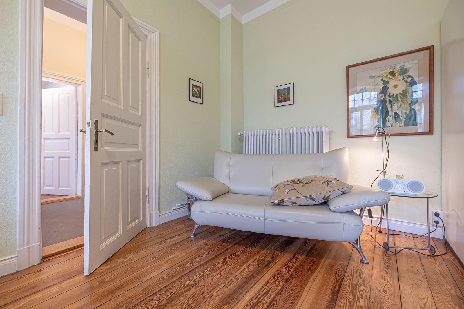 Ein Raum mit einem weißen Sofa, Holzboden und einer Tür zum Flur.