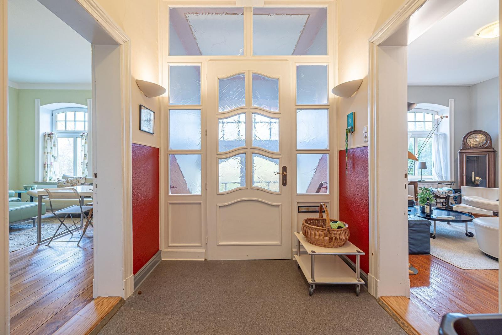 Eingang mit Glasfronttür, roten Wänden und Blick in Wohn- und Essbereich.