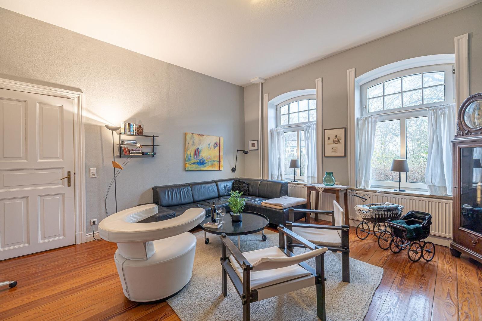 Wohnzimmer mit Sofa, Stühlen, Tisch und Fenstern mit weißen Vorhängen.