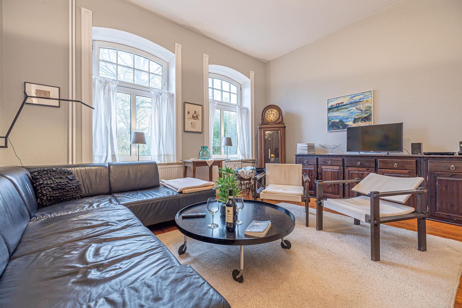 Ein Wohnzimmer mit Ledersofa, zwei Sesseln und zwei großen Fenstern.