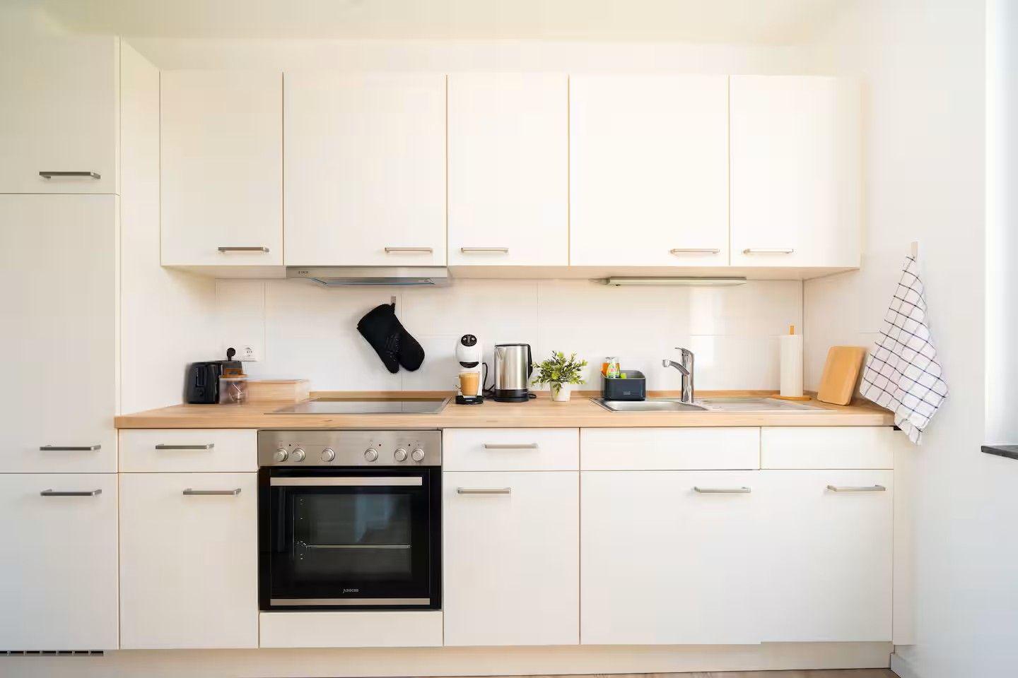 Küche mit weißen Schränken, Holzoberfläche und integriertem Backofen.