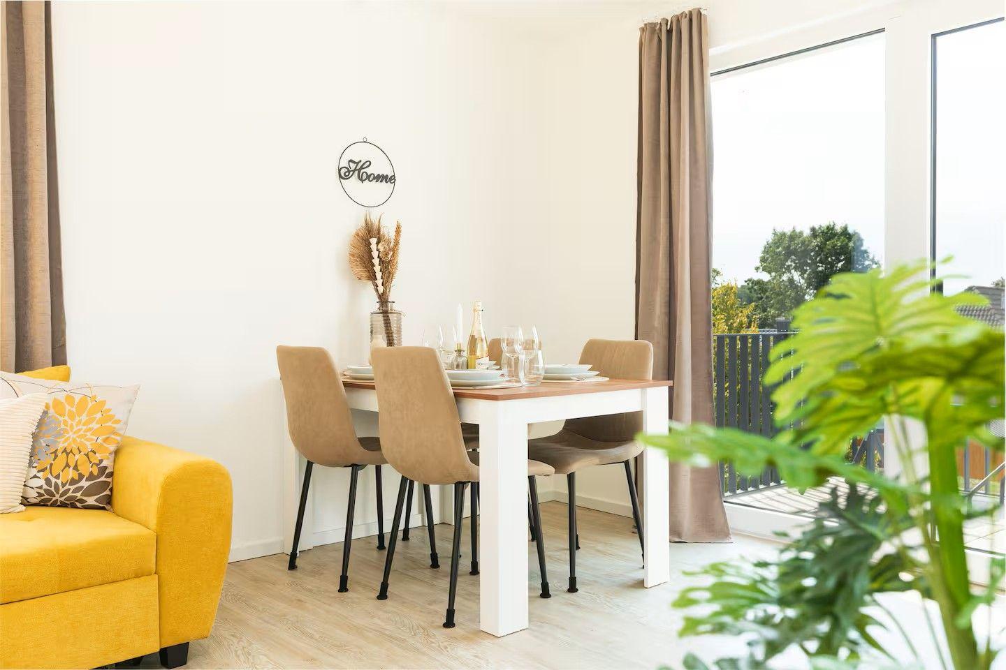 Essbereich mit Tisch, Stühlen und Blick auf Balkon. Gelber Sessel und Pflanze im Vordergrund.