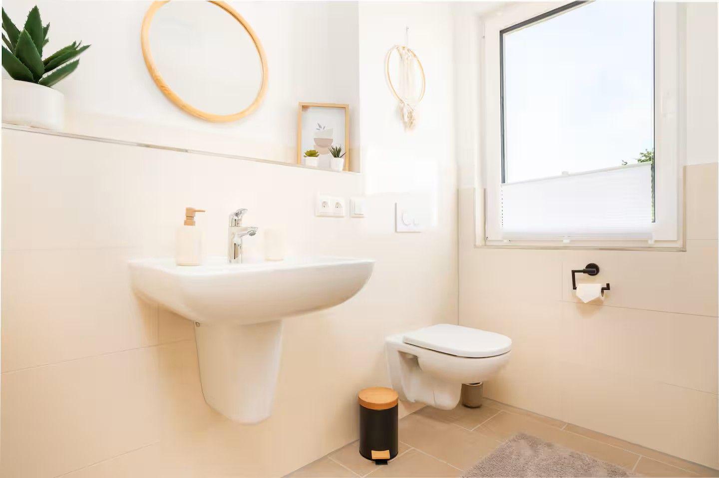 Badezimmer mit Waschbecken, Toilette und Fenster. Dekoration mit Pflanzen und Spiegel.