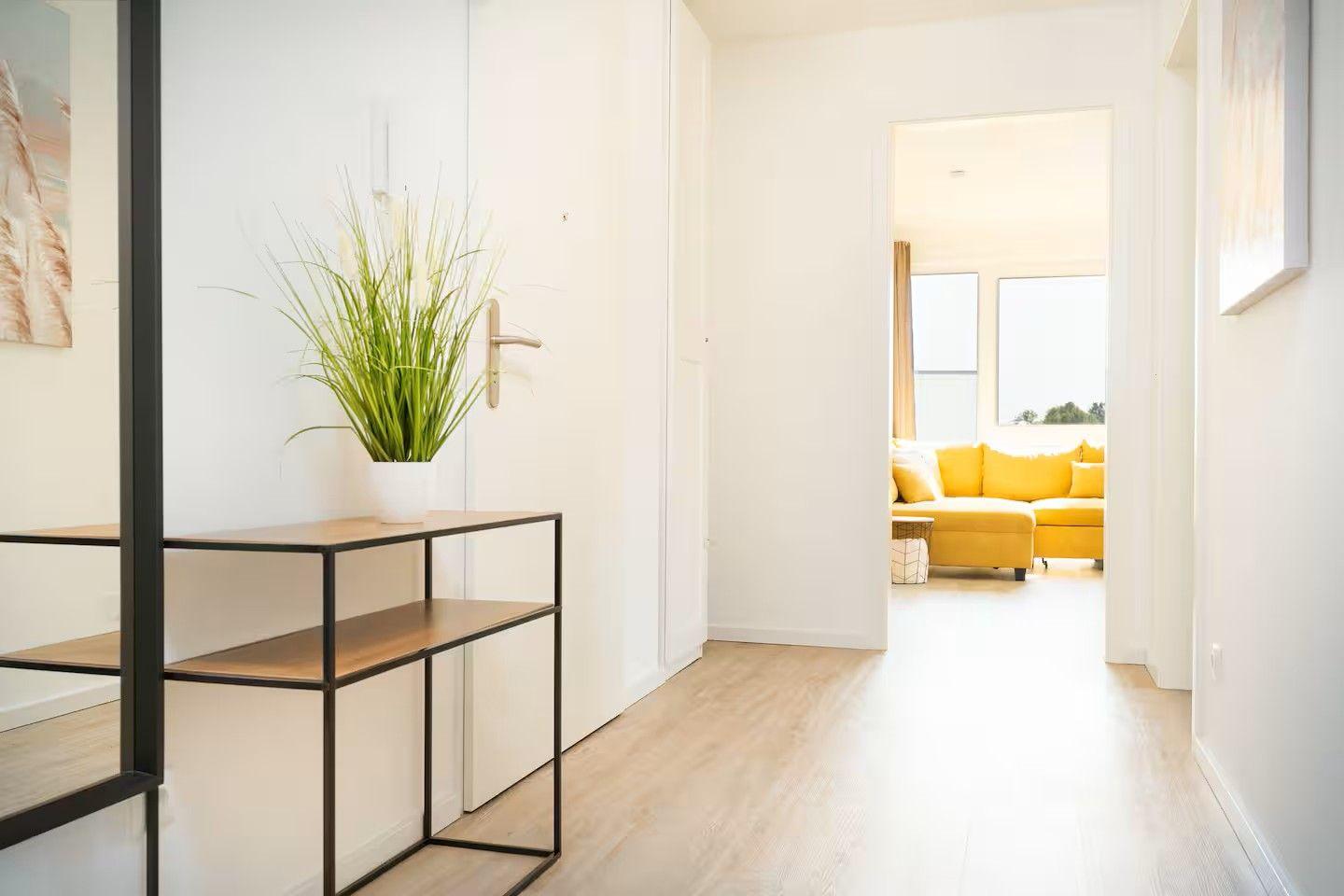 Flur mit Pflanze und Tisch, Blick in Wohnzimmer mit gelbem Sofa.