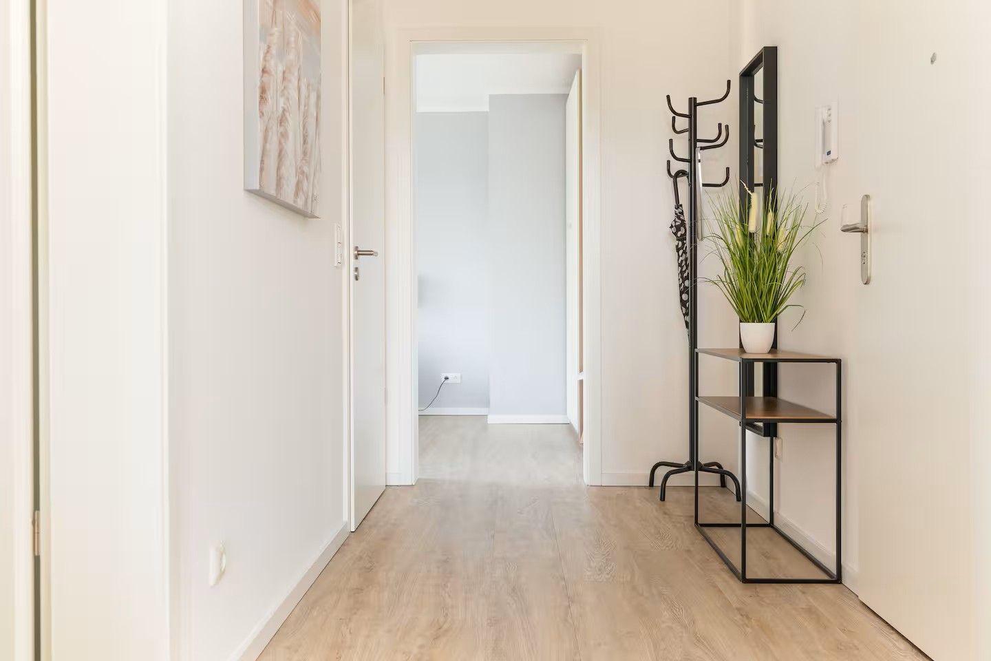 Flur mit Holzboden, Kleiderständer, Pflanze und Spiegel an der Wand.