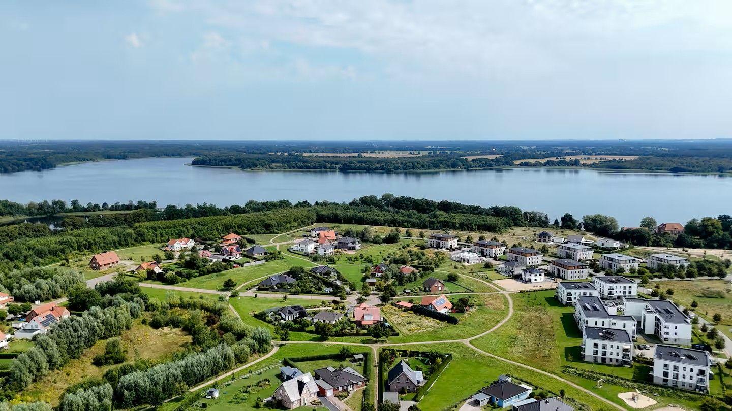 Luftbild von Wohnhäusern am See mit grünen Wiesen und Bäumen im Hintergrund.