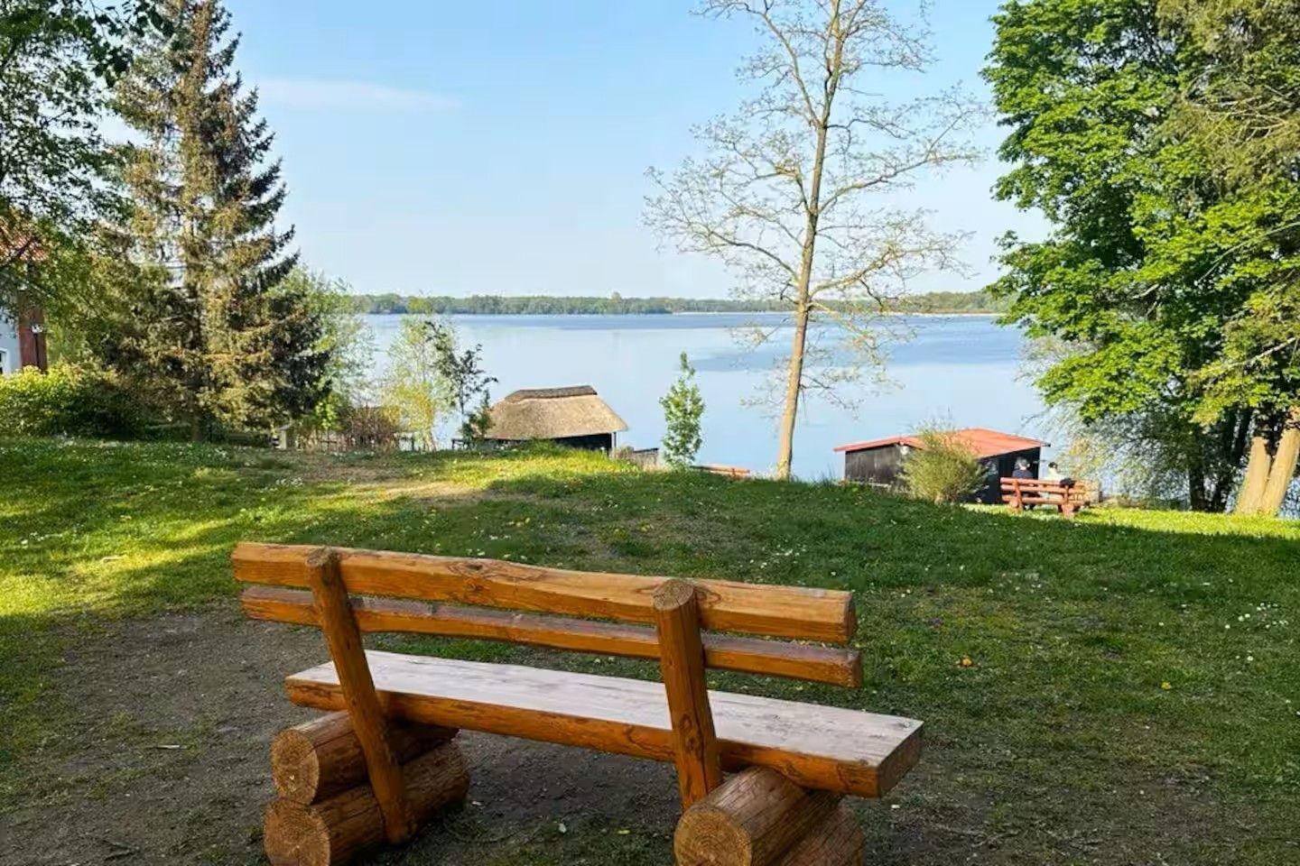 Holzbank am Seeufer mit Blick auf Wasser und Bäume.