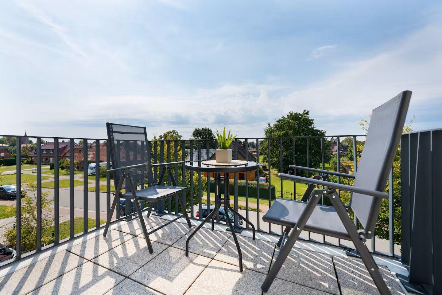 Terrasse mit zwei Stühlen und Tisch, Blick auf Wohngebiet und Bäume.