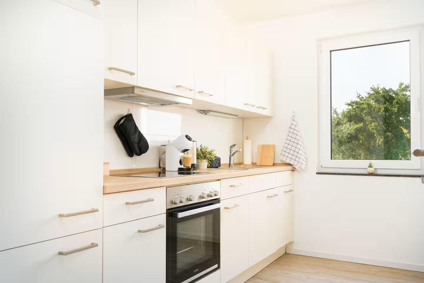Küche mit weißen Schränken, Holzoberfläche und Fenster mit Blick auf Bäume.