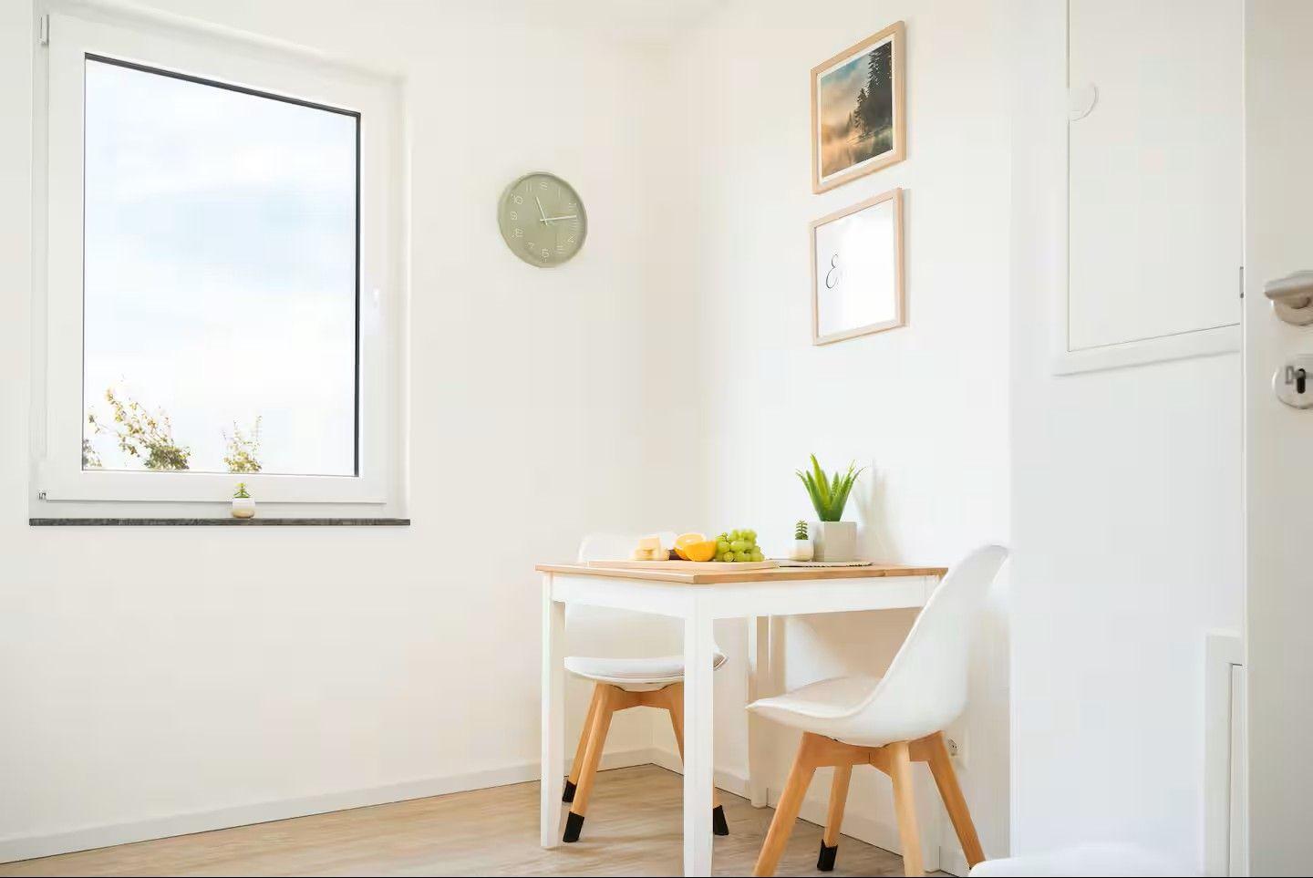 Kleiner Essbereich mit Tisch, zwei Stühlen, Wanduhr und Fenster.