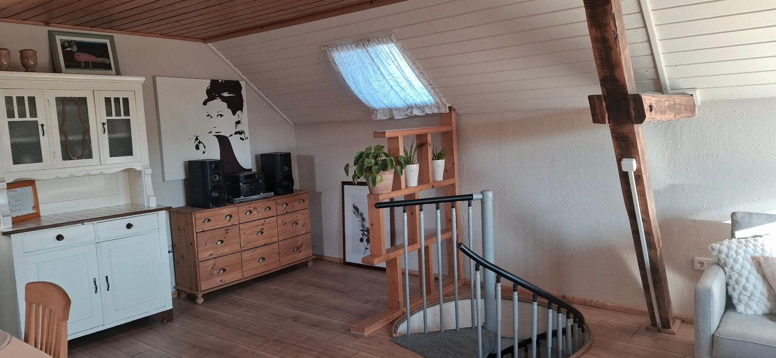 Dachgeschosswohnung mit Holzboden, Treppe, Pflanzenregal und Küchenzeile.