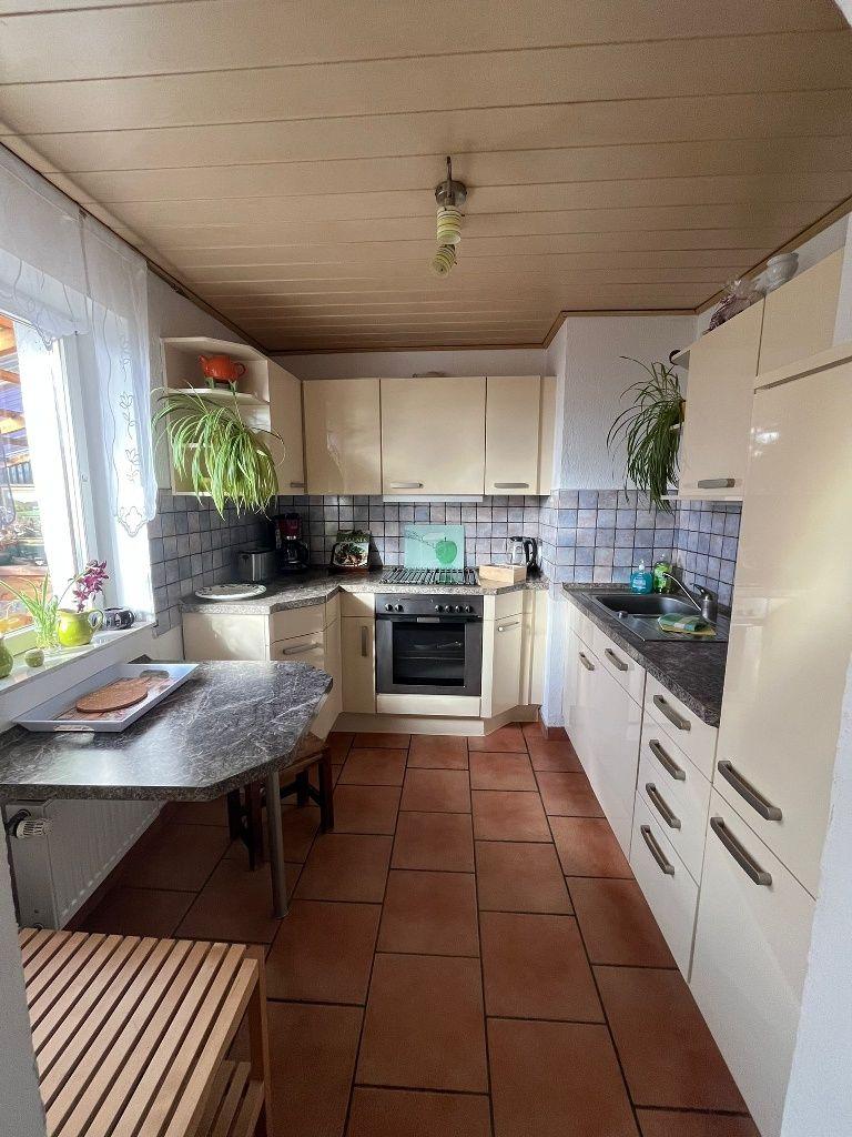 Küche mit Arbeitsplatten, Spüle, Herd und Fenster. Holzdecke und Fliesenboden.