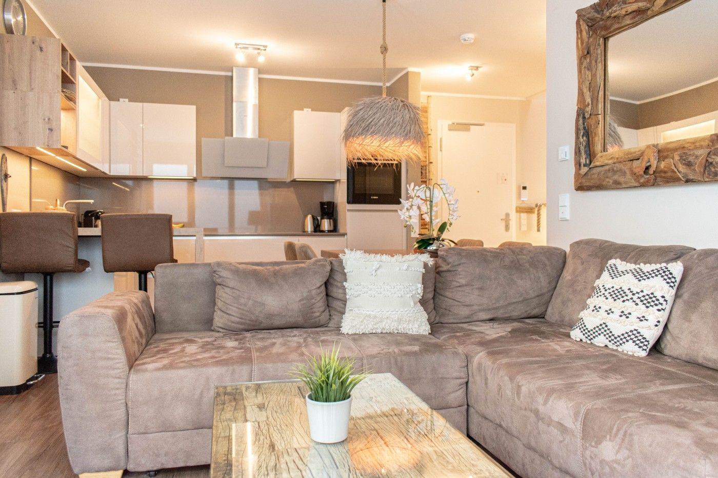 Wohnbereich mit Sofa, Couchtisch und Küche im Hintergrund.