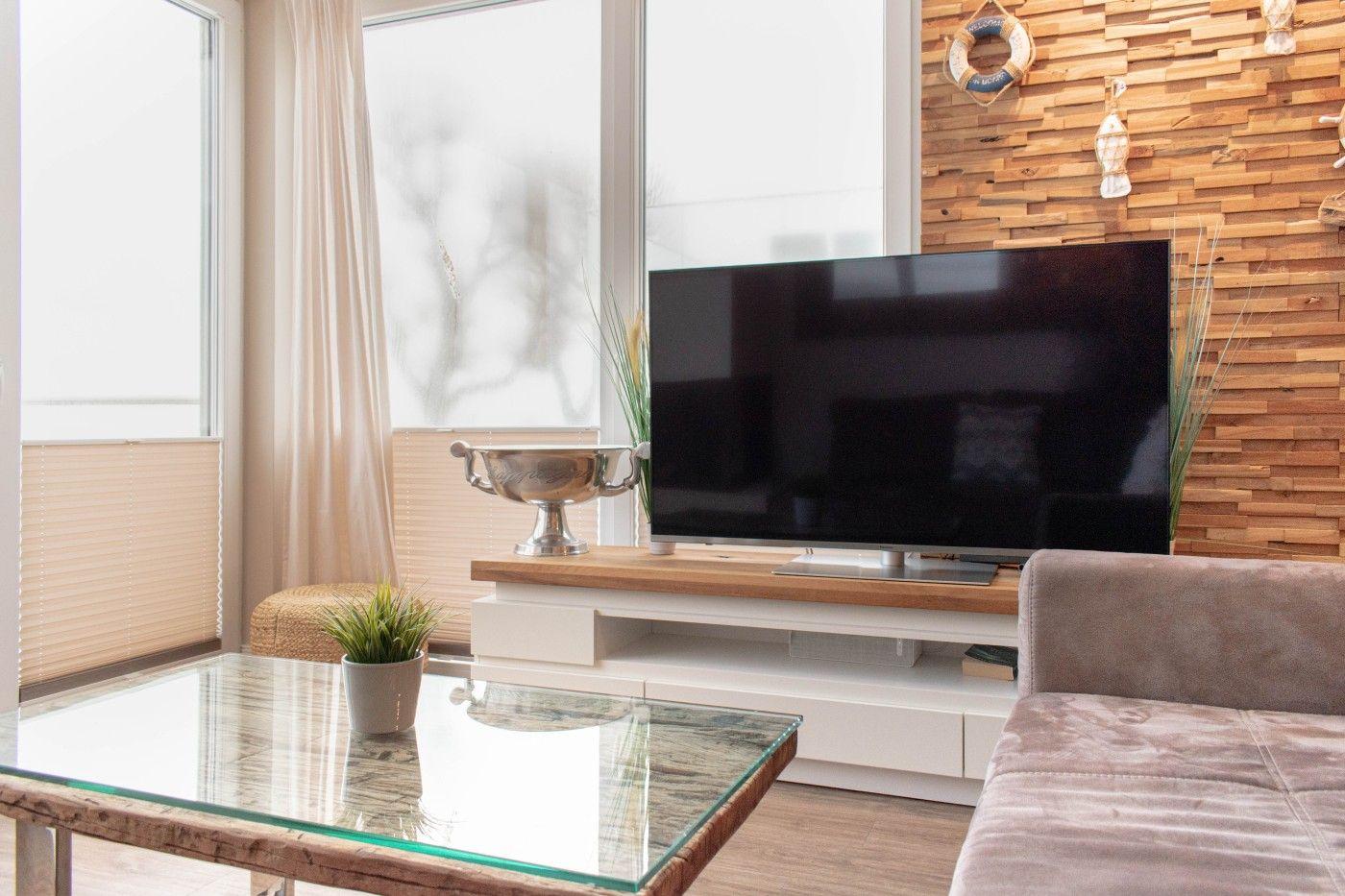 Wohnzimmer mit Fernseher, Glas-Tisch und Holzwand.