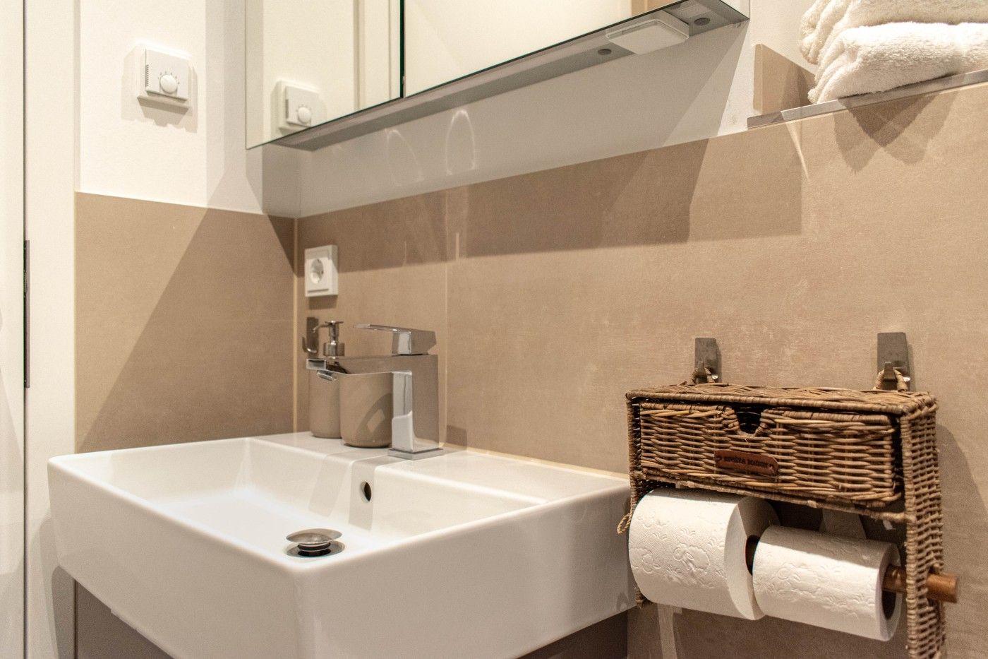 Bad mit Waschbecken, Spiegel und Toilettenpapierhalter.