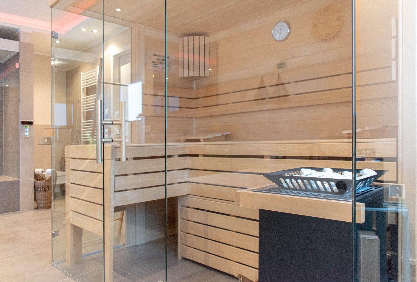 Sauna mit Holzbank und Glaswand. Auf dem Tisch liegen weiße Steine.