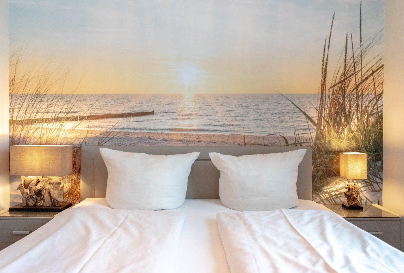Schlafzimmer mit Bett, Kissen und Wandbild von Strand und Meer.