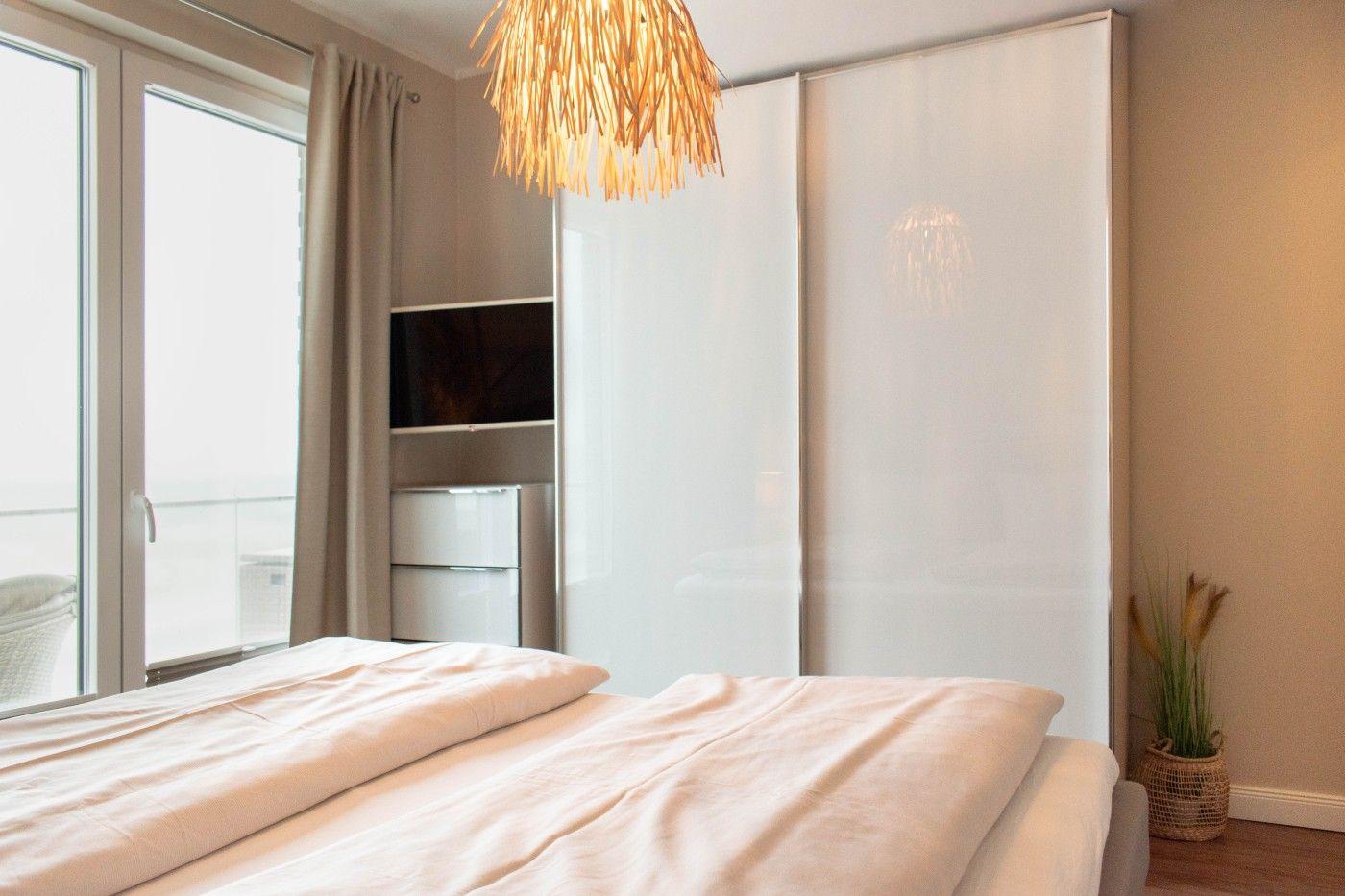 Schlafzimmer mit Bett, Schwebetüren-Schrank und Fenster zur Terrasse.