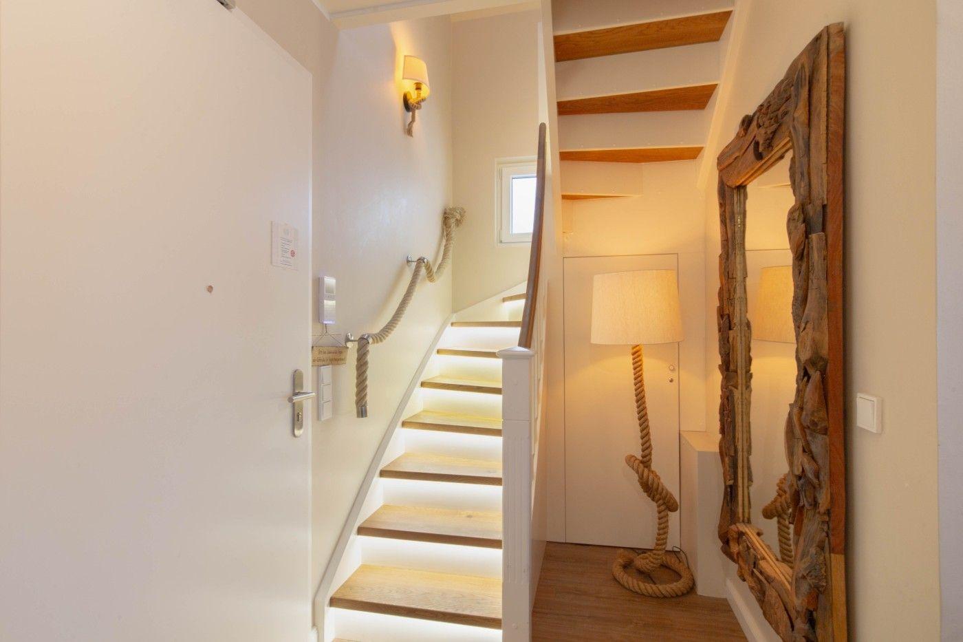 Hausflur mit Treppe, Seilgeländer und grobem Holzspiegel.