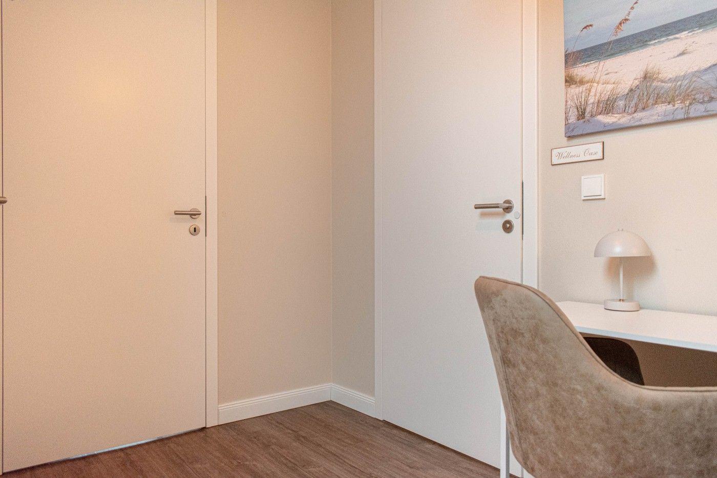 Wohnraum mit Schreibtisch, Stuhl und Wandbild. Zwei Türen und Holzboden.