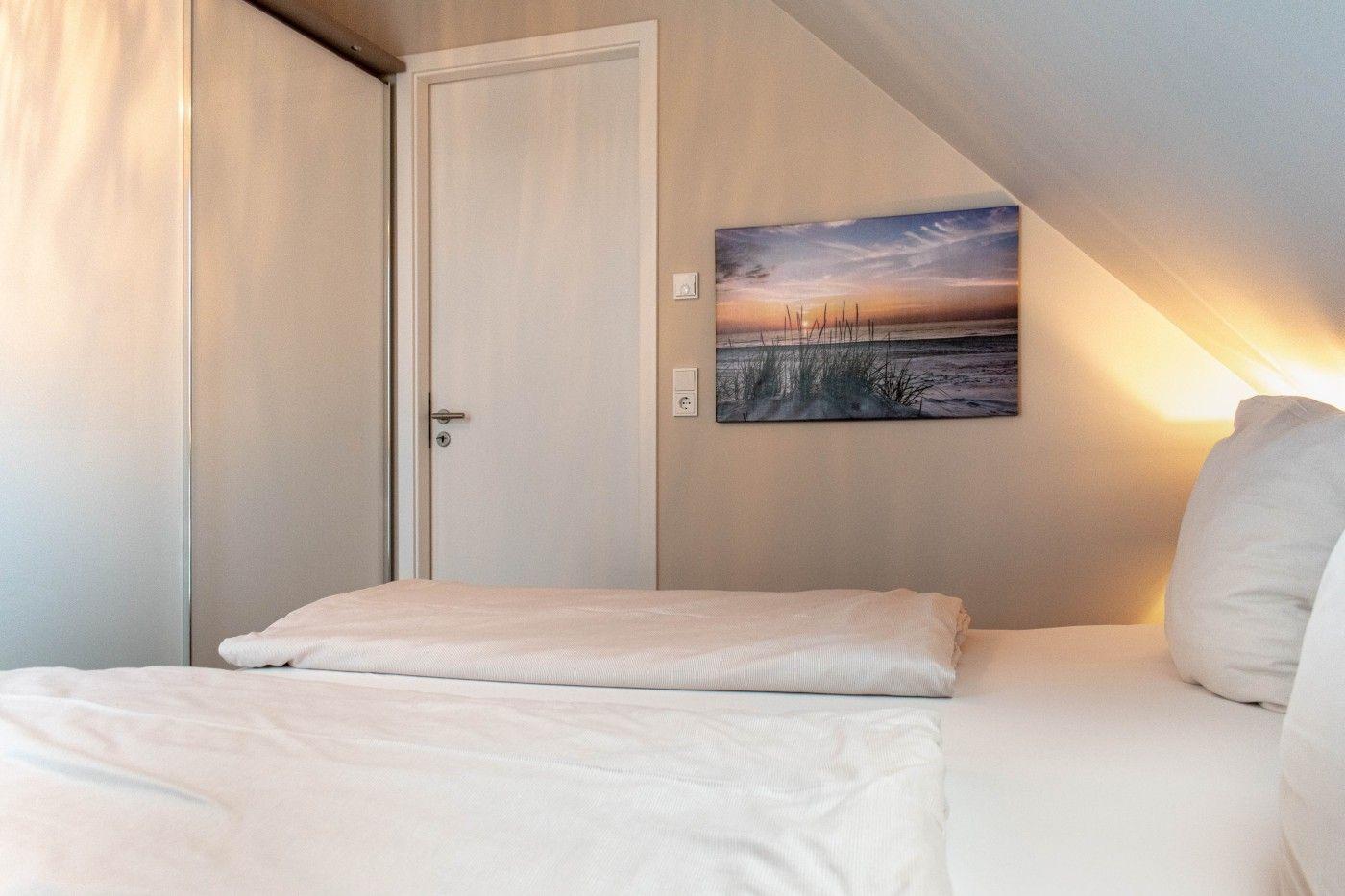 Schlafzimmer mit Bett, Wandbild und Schiebetüren unter Dachschrägen.