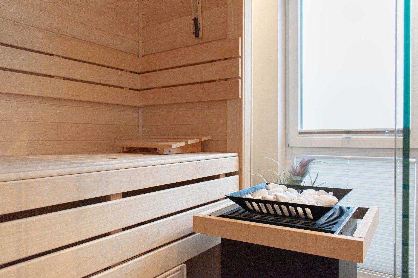 Sauna mit Holzbank und Steinkorb vor Fenster
