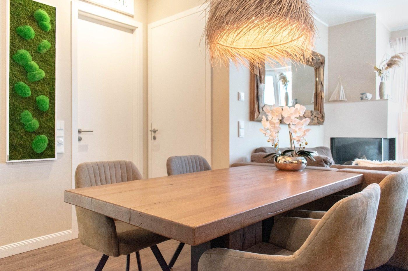 Esszimmer mit Holztisch, Stühlen und Deckenleuchte. Im Hintergrund Wohnzimmer mit Kamin.