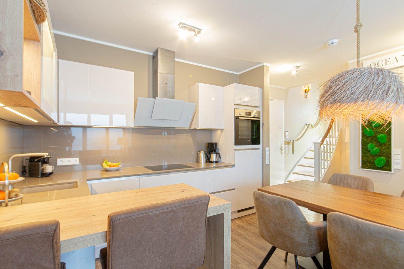 Küche mit Essbereich, Holztische und Stühle, weiße Schränke und integrierte Geräte.