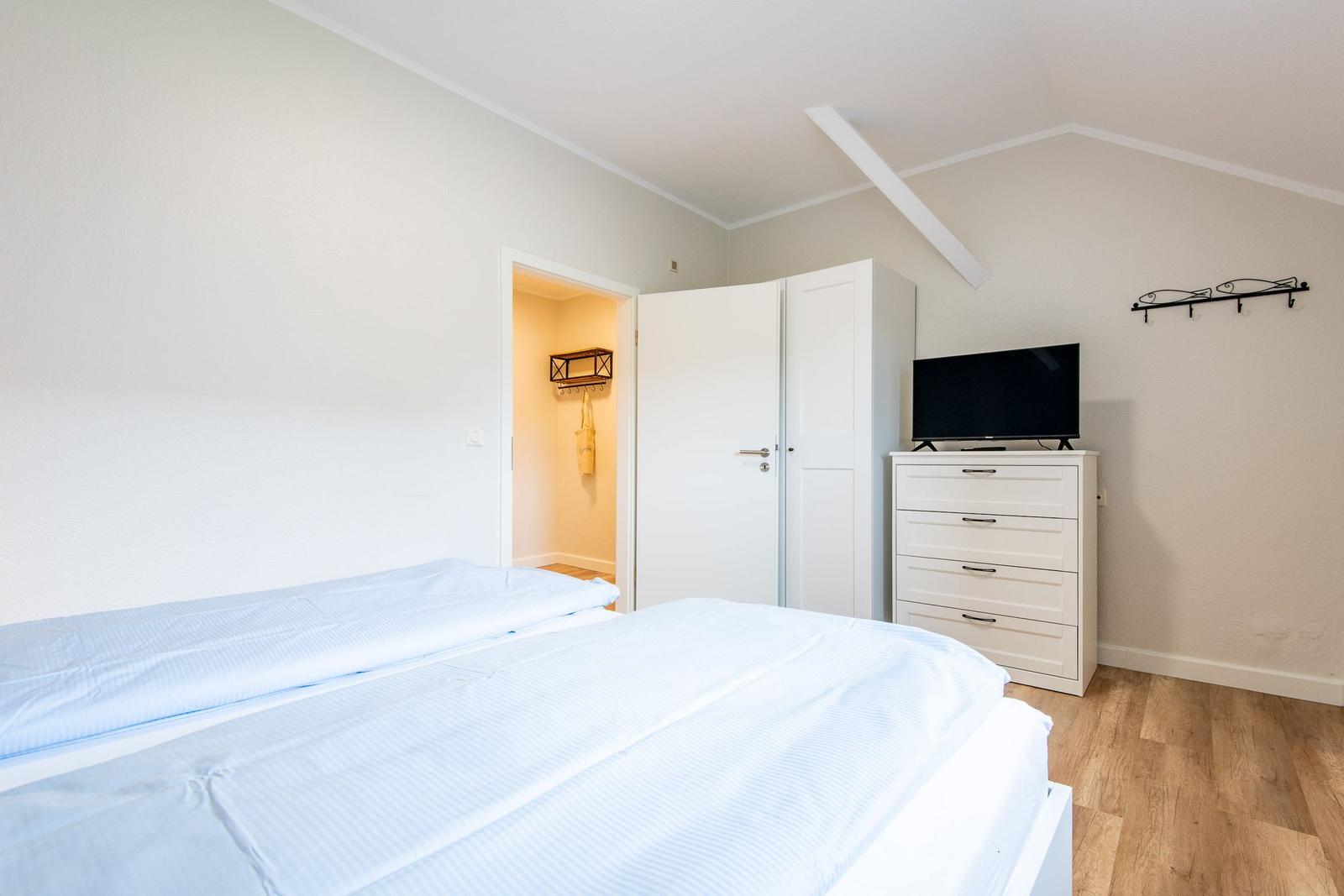Schlafzimmer mit Bett, Schrank und Fernseher. Holzboden und Dachschräge.