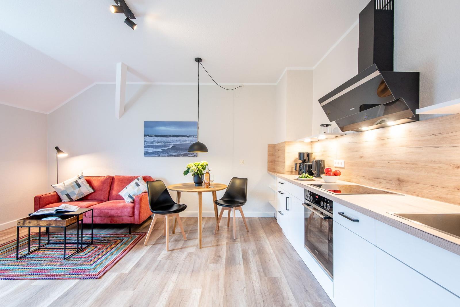 Wohnküche mit rotem Sofa, Esstisch und moderner Küchenzeile.