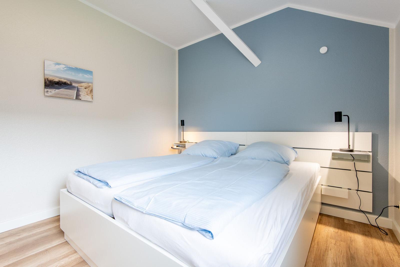 Schlafzimmer mit Doppelbett, blauer Wand und Nachttischen.