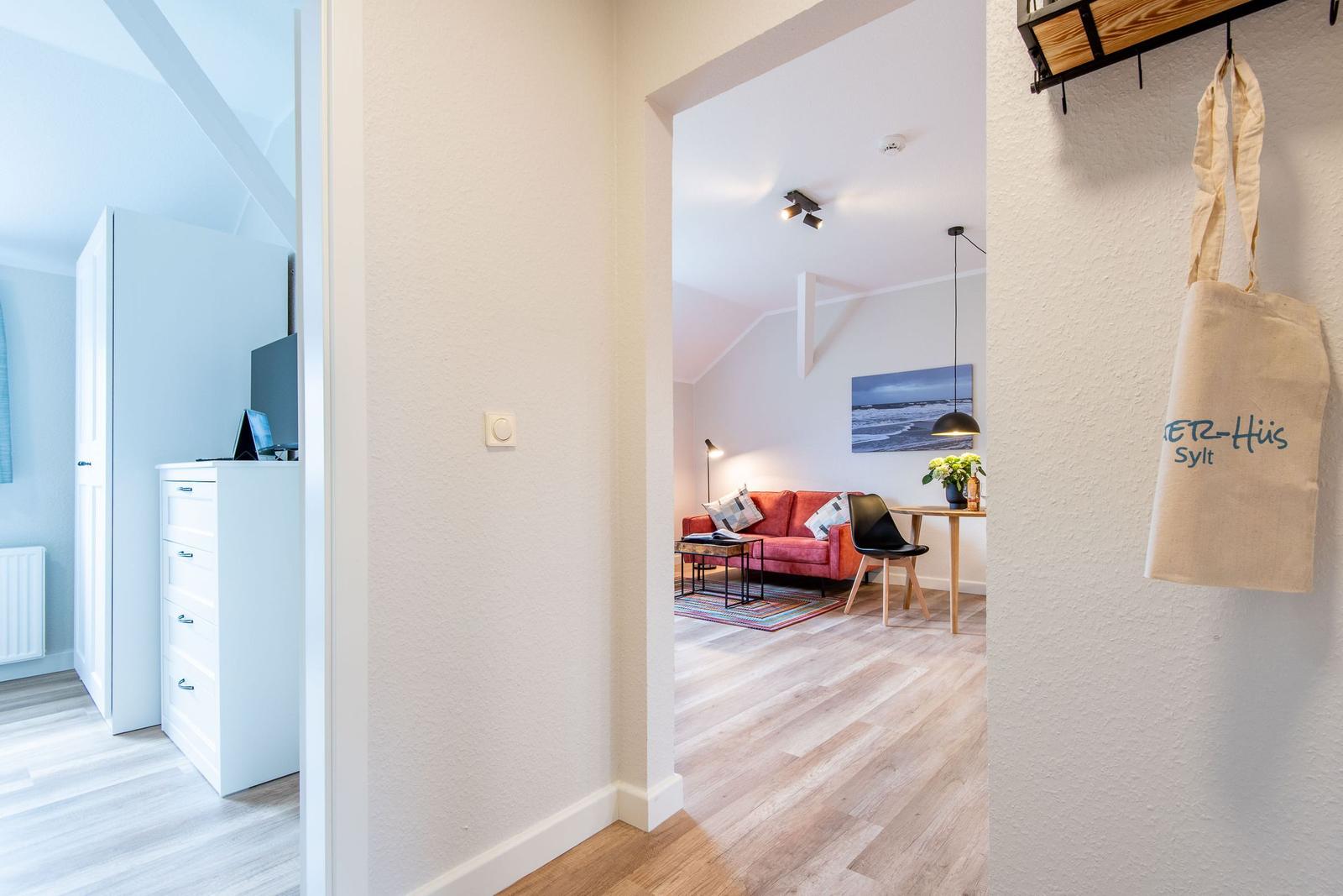 Wohnbereich mit rotem Sofa und Essplatz. Nebenraum mit Schrank und TV.