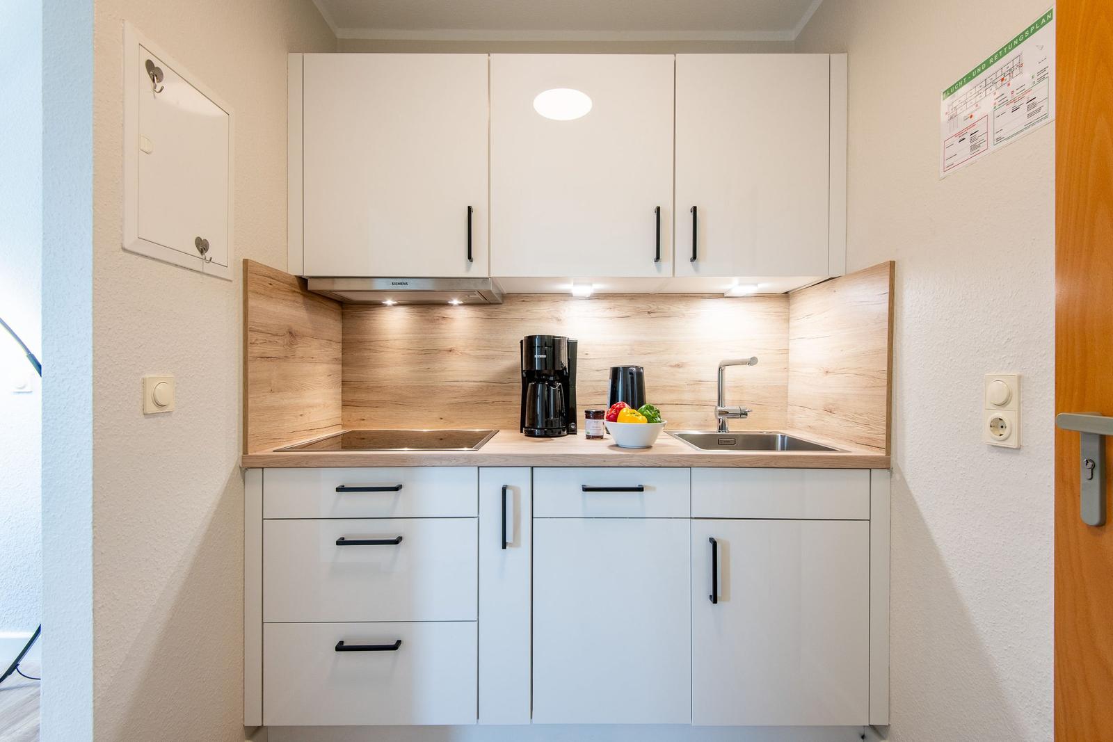 Küche mit weißen Schränken, Holzrückwand und Edelstahlspüle.